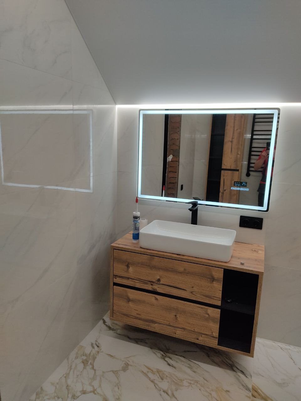Wooden vanity unit and a backlit mirror in a renovated bathroom