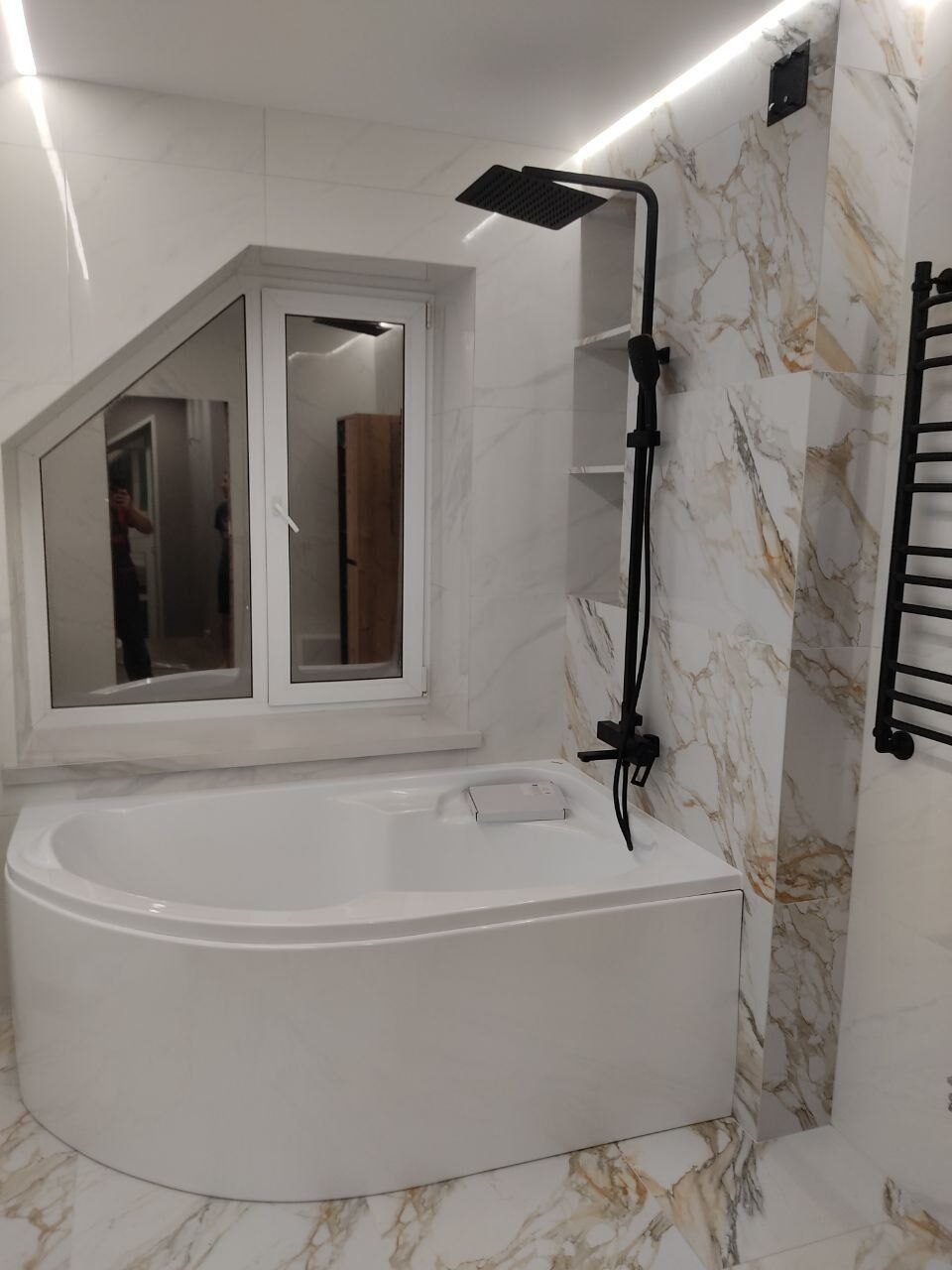 Corner bathtub under a window with black fittings after a bathroom renovation