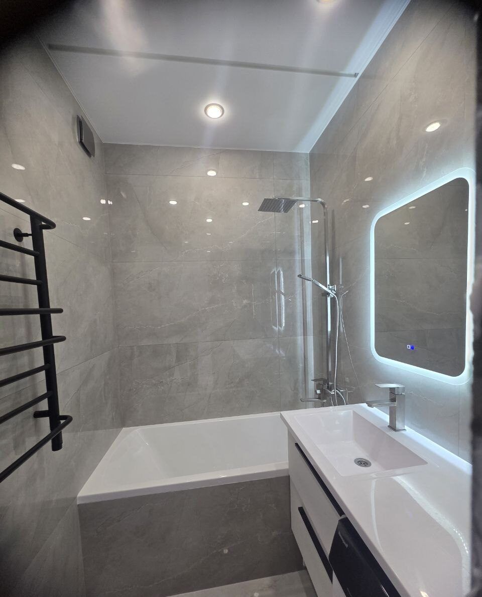 Grey bathroom with a bathtub and a backlit mirror after renovation