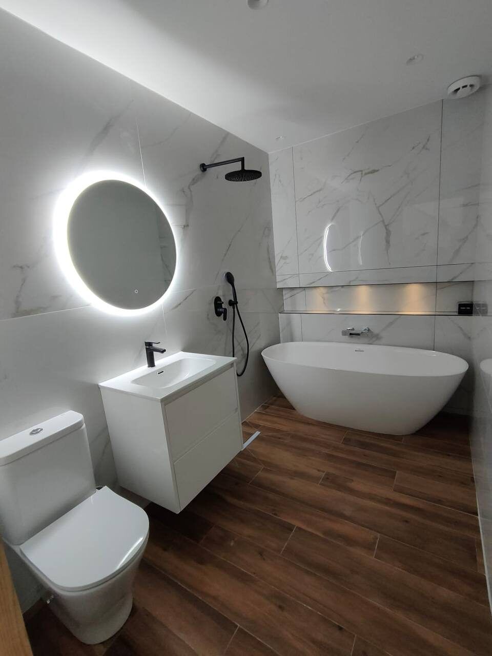 Bathroom with a freestanding bathtub, round mirror and wooden floor after renovation