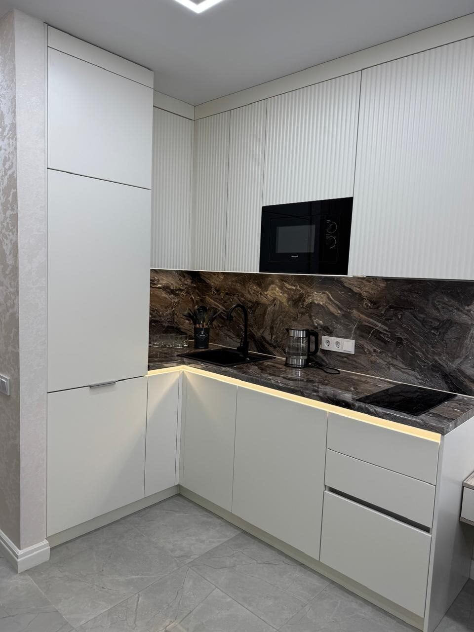 White kitchen unit with a dark stone splashback after a studio renovation