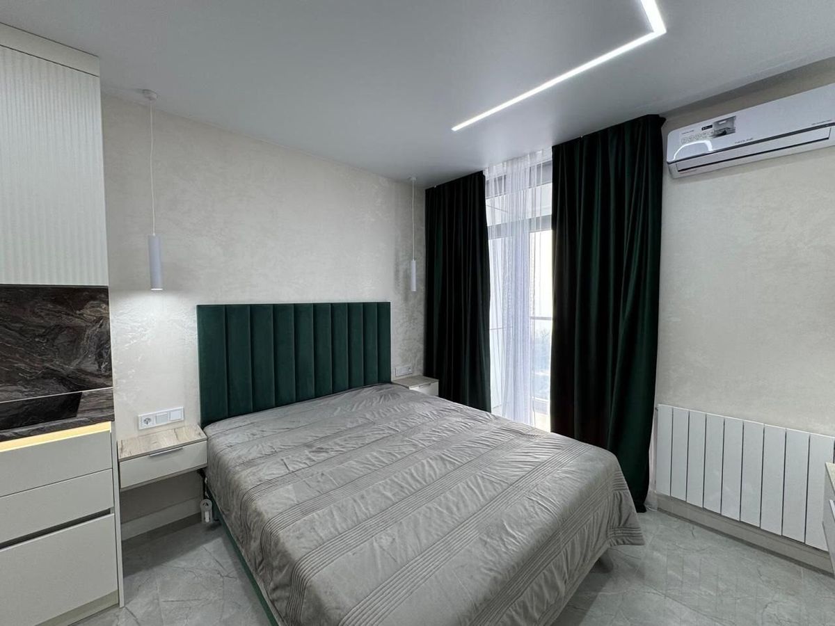 Bed with a green upholstered headboard by a window with green curtains, Prague