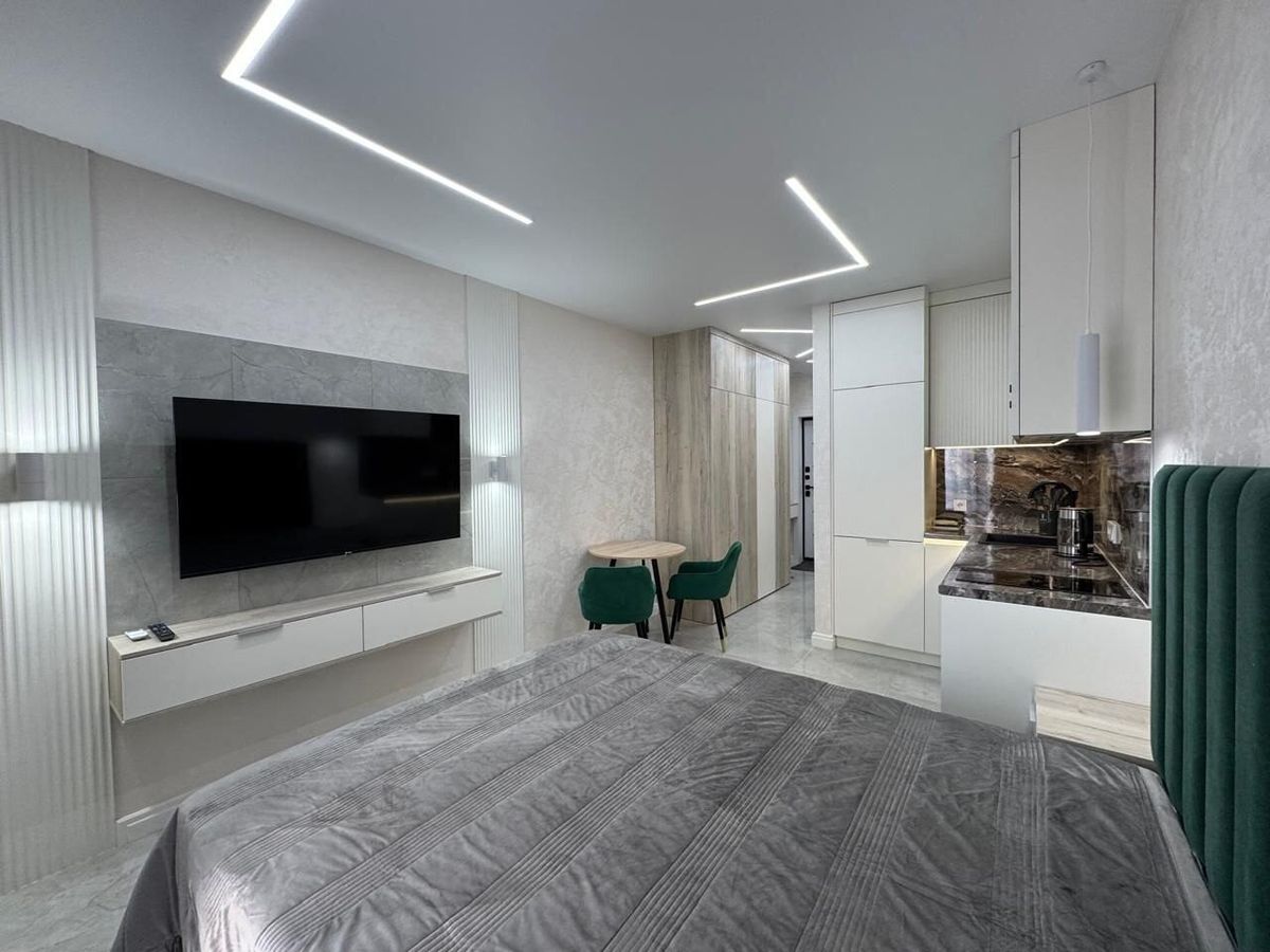 TV wall, bed and a dining corner with green chairs in a renovated studio apartment