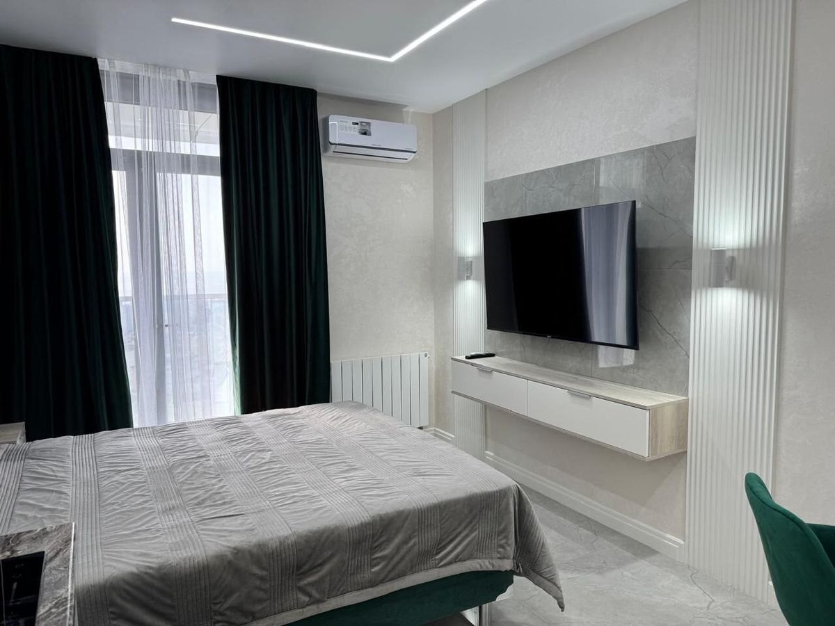 TV wall and bed in a renovated studio apartment with green curtains