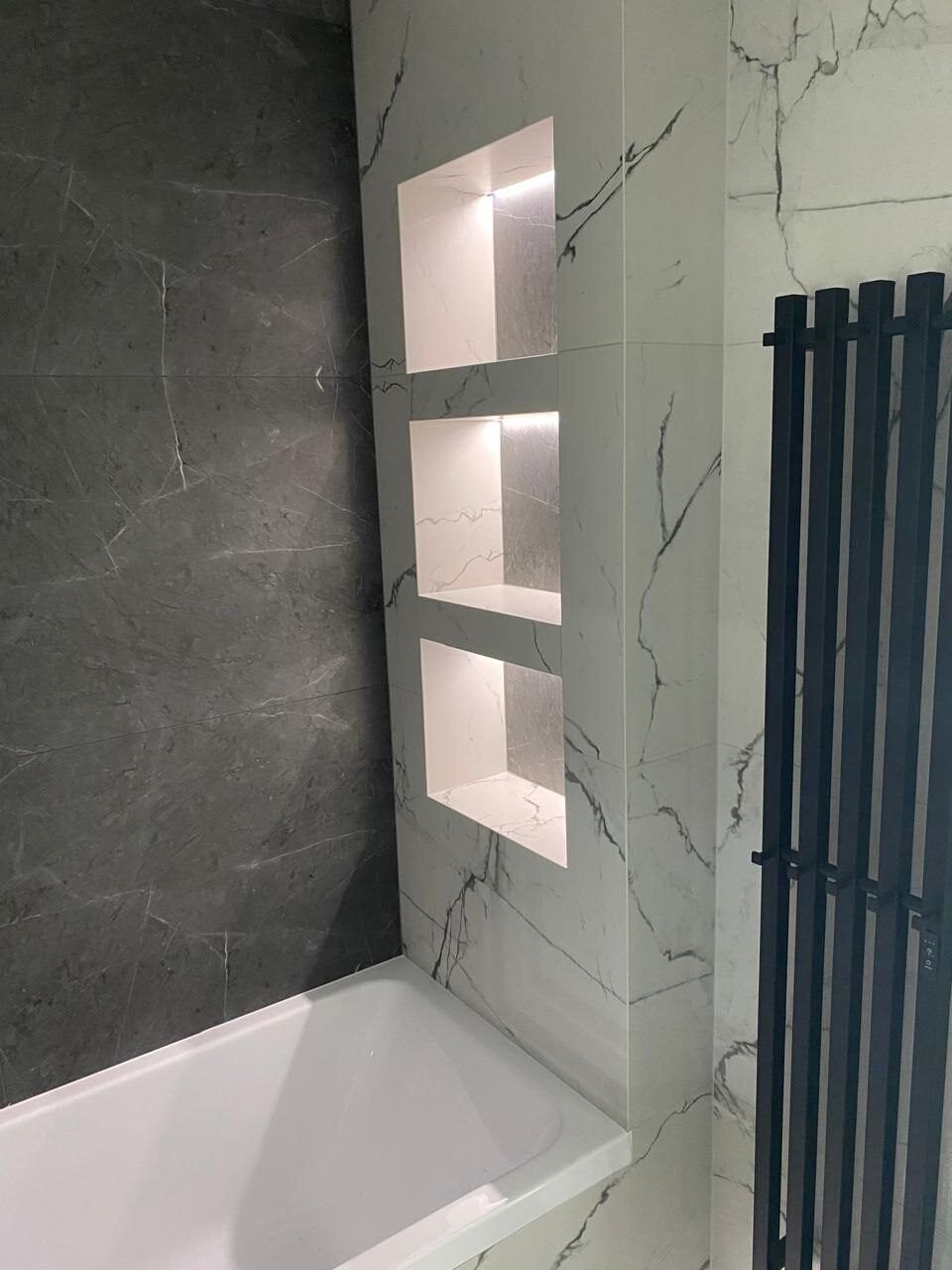 Backlit wall niches and a black designer radiator in a renovated bathroom
