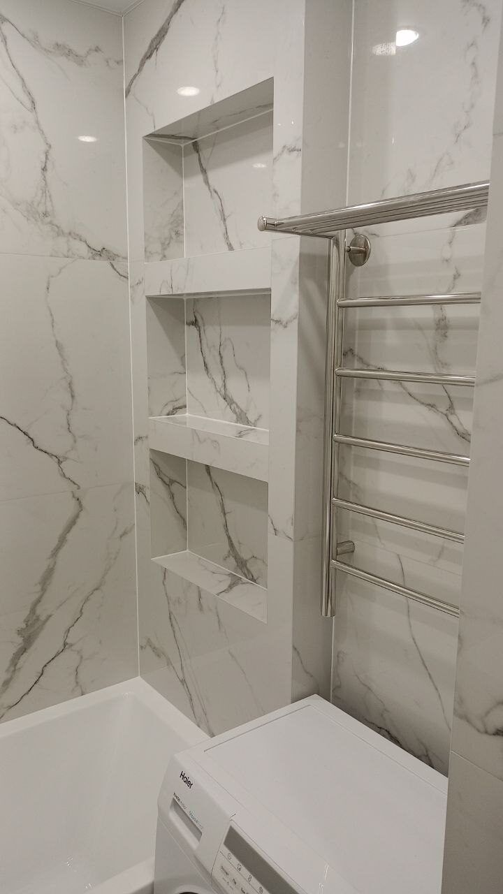 Bathtub with built-in niches and a towel rail in a white marble bathroom