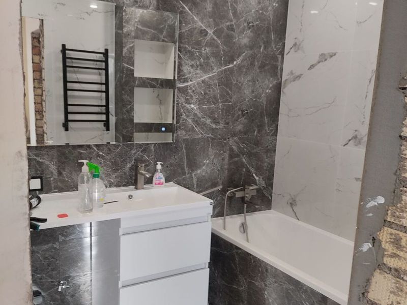 Bathroom with marble-effect tiling and a bath after a Prague flat renovation