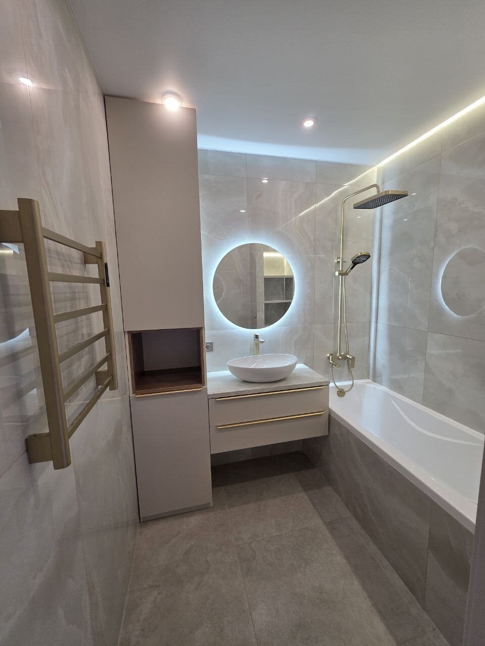 Renovated bathroom with a gold towel rail, round mirror and bathtub, Prague
