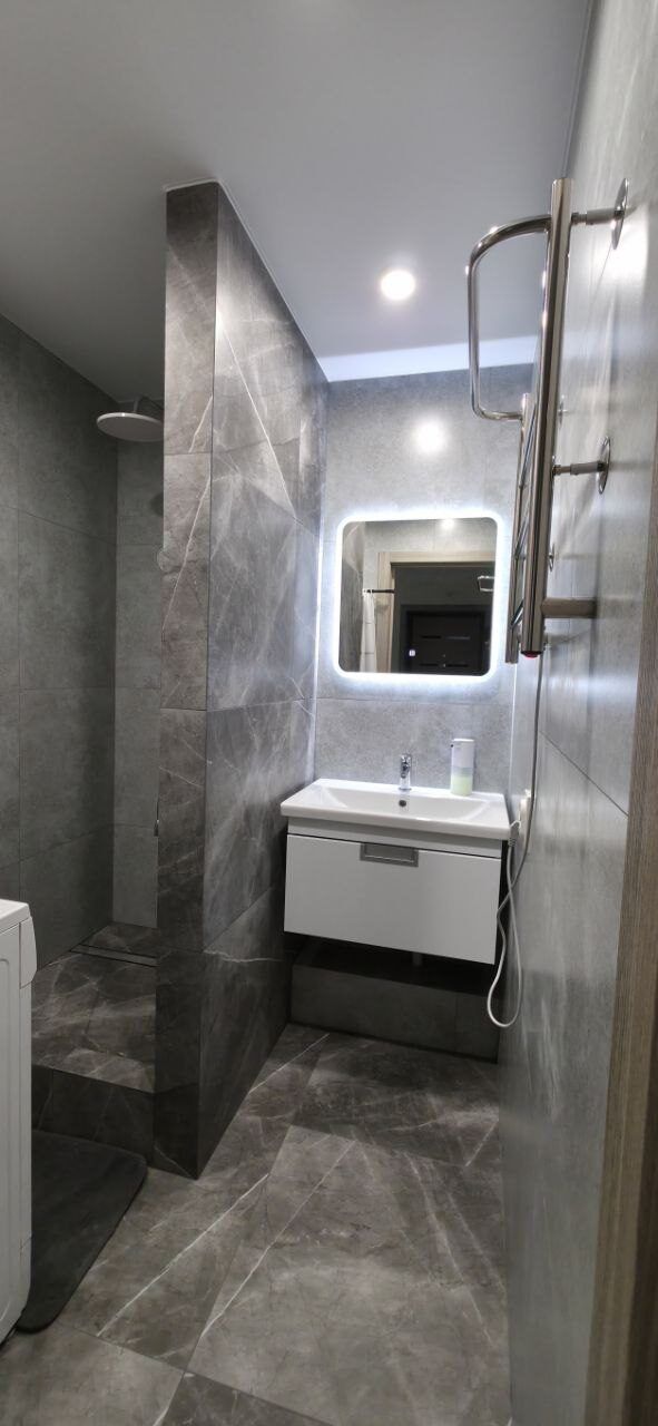 Finished shower enclosure with grey tiling and a backlit mirror